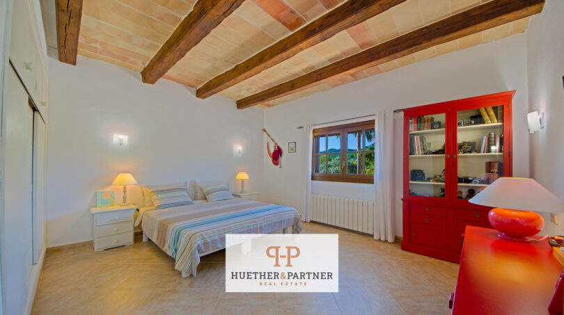 Dormitorio luminoso de la finca Felanitx con techo de vigas de madera, armario rojo y cama doble