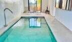 Elegant indoor pool with turquoise water, natural stone flooring and panoramic windows in high-quality finca in Campos