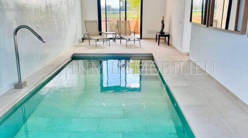 Elegant indoor pool with turquoise water, natural stone flooring and panoramic windows in high-quality finca in Campos