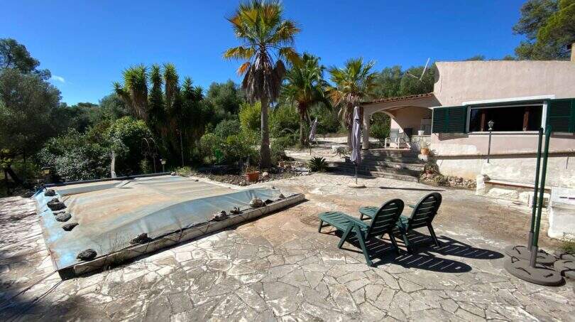 Mediterraner Außenbereich der Finca in Algaida mit abgedecktem Pool, Steinboden, Liegestühlen und Palmen.