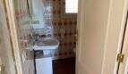Pequeño baño con papel tapiz retro estampado, lavabo y suelo de terracota en finca mediterránea.