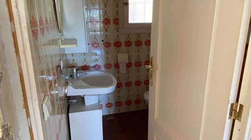 Pequeño baño con papel tapiz retro estampado, lavabo y suelo de terracota en finca mediterránea.