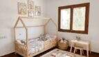 Habitación infantil de la finca en Algaida con cama tipo casa, alfombra de juegos y lámpara de pantalla de globo aerostático encantadora.