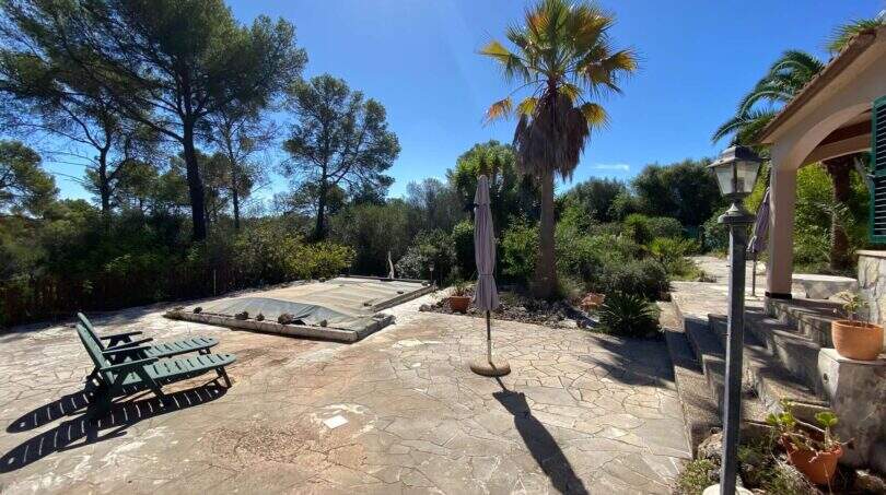 Mediterraner Außenbereich der Finca in Algaida mit abgedecktem Pool, Natursteintetrasse, Palmen und Liegestühlen.