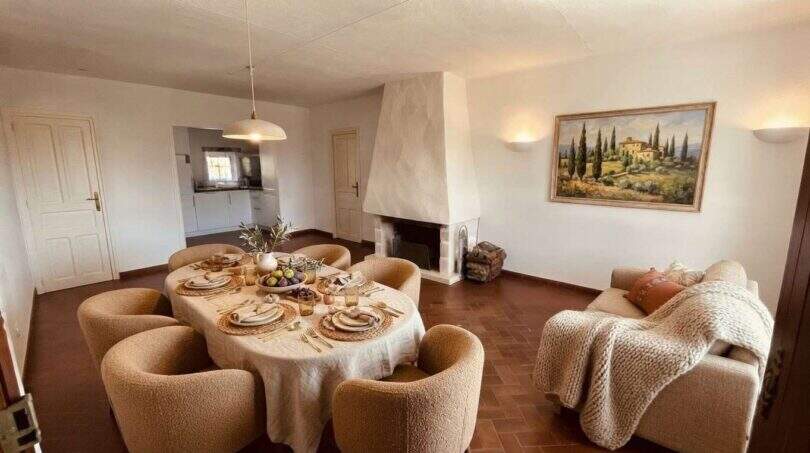 Luminosa sala-comedor de la finca con mesa de comedor puesta, chimenea, sofá y pintura mediterránea.