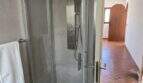 Modernes Duschbad der mediterranen Finca mit Glaskabine, Regendusche und Terrakottaboden im Flurbereich.