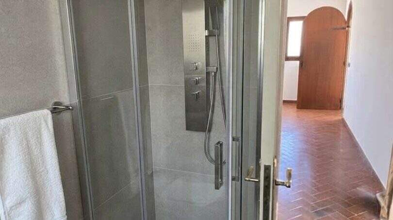 Modernes Duschbad der mediterranen Finca mit Glaskabine, Regendusche und Terrakottaboden im Flurbereich.