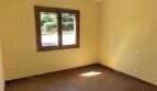 Habitación vacía de la finca en Algaida con paredes amarillas, suelo de baldosas marrones y pequeña ventana al jardín.