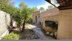 Ungepflegter Innenhof der mediterranen Finca in Algaida mit Yucca-Palme, Kiesweg und Nebengebäude.