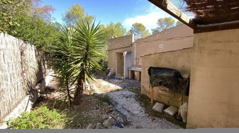 Ungepflegter Innenhof der mediterranen Finca in Algaida mit Yucca-Palme, Kiesweg und Nebengebäude.