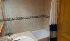 Badezimmer der Ruheoase in Porto Cristo mit Marmor-Waschtisch, Badewanne und blau-weißem Duschvorhang.
