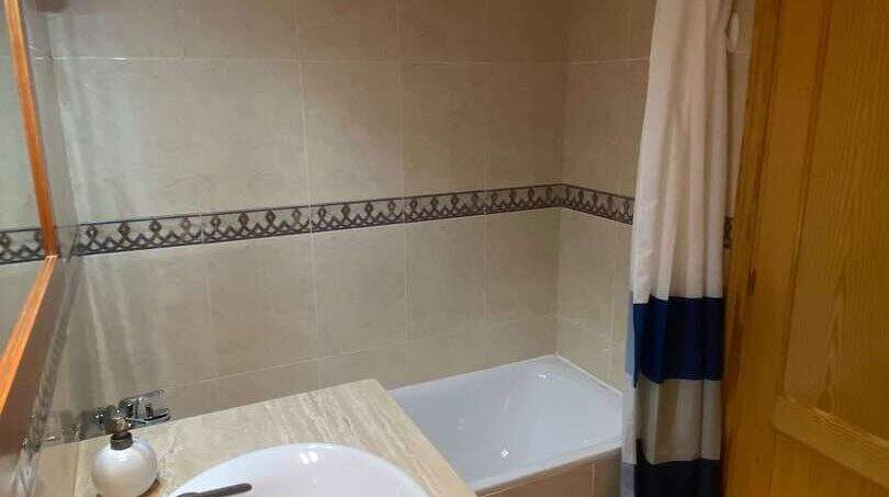 Badezimmer der Ruheoase in Porto Cristo mit Marmor-Waschtisch, Badewanne und blau-weißem Duschvorhang.