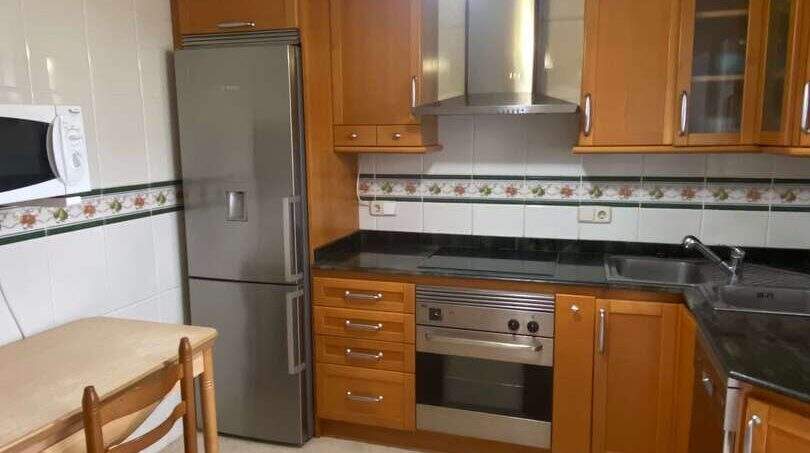 Küche der Ruheoase in Porto Cristo mit Holzschränken, Einbauofen, Kühlschrank und Esstisch.