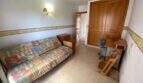 Helles Zimmer mit buntem Schlafsofa, Holzschrank, Schreibtisch und Stuhl in Ruheoase Porto Cristo.