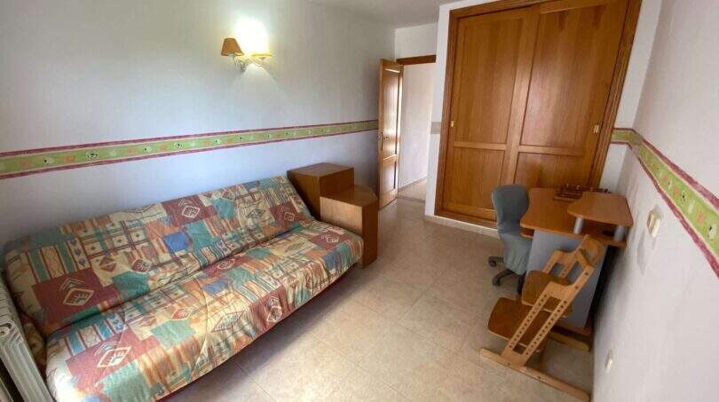 Helles Zimmer mit buntem Schlafsofa, Holzschrank, Schreibtisch und Stuhl in Ruheoase Porto Cristo.