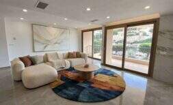 Bright living room with boucle sofa, colorful rug and panoramic sliding doors with harbor view in Porto Cristo.