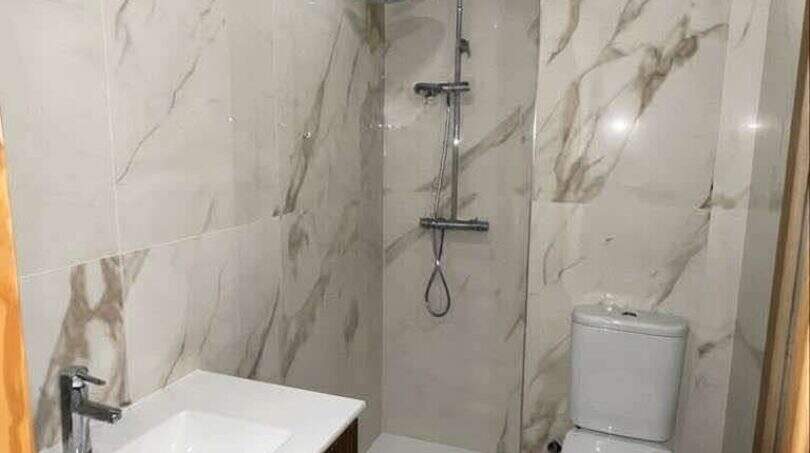 Modernes Badezimmer mit Marmoroptik-Fliesen, Walk-in-Dusche, WC und Holz-Waschtisch in Porto Cristo.