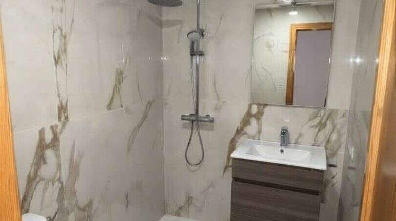 Modernes Badezimmer mit Marmoroptik-Fliesen, bodenebener Dusche, schwebendem Waschtisch und WC in Hafenwohnung Porto Cristo