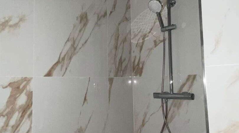 Modernes Duschsystem in Chromoptik mit Regendusche vor eleganten Marmorfliesen in der Hafenwohnung Porto Cristo
