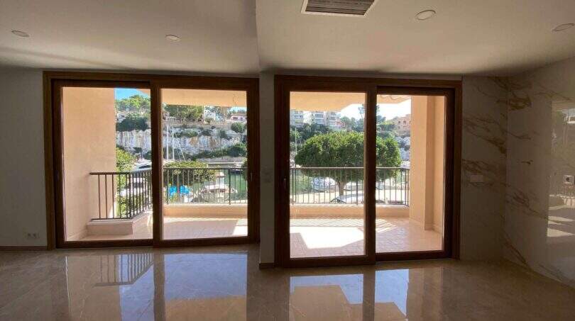 Heller Wohnraum mit Marmorböden und zwei Glasschiebetüren zum Balkon mit Hafenblick in Porto Cristo
