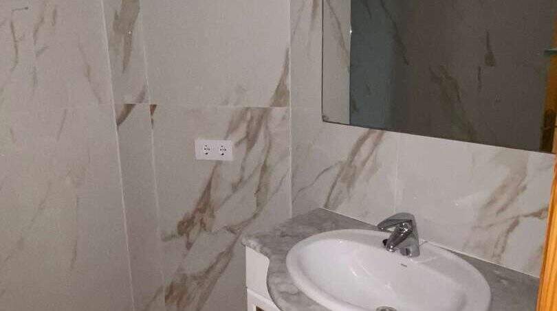 Elegantes Badezimmer mit Marmorwänden, weißem Waschtischunterschrank und großem Spiegel in Hafenwohnung Porto Cristo
