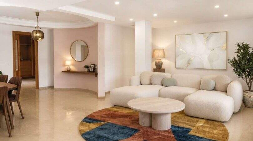 Helles Wohnzimmer mit weißem Bouclé-Sofa, buntem Rundteppich und modernem Couchtisch in exklusiver Hafenwohnung