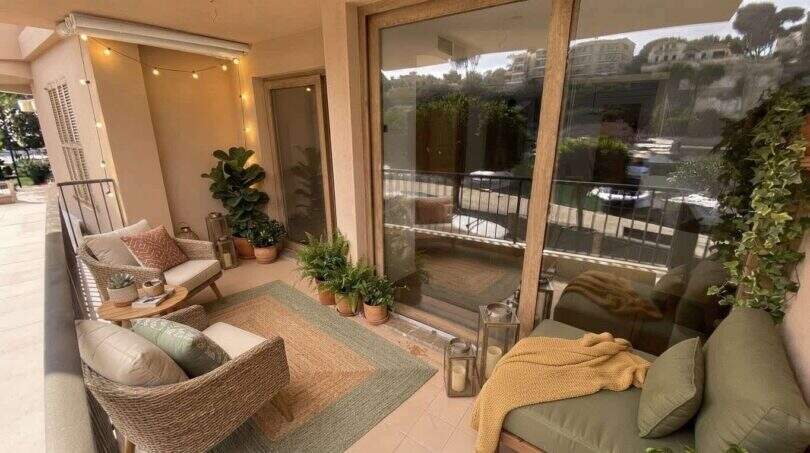 Gemütliche Balkonterrasse der Hafenwohnung Porto Cristo mit Rattanmöbeln, Pflanzen und Lichterketten
