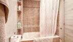 Badezimmer mit Mosaikfliesen, Badewanne, Duschvorhang und Einbauregal in strandnaher Wohnung in Palma