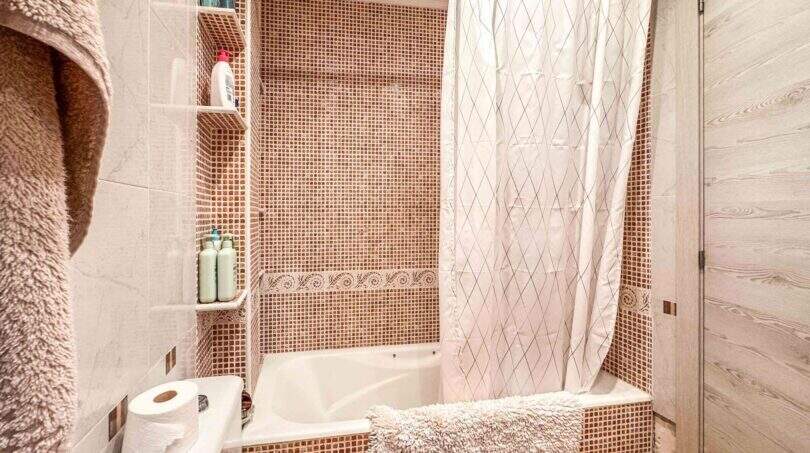 Badezimmer mit Mosaikfliesen, Badewanne, Duschvorhang und Einbauregal in strandnaher Wohnung in Palma