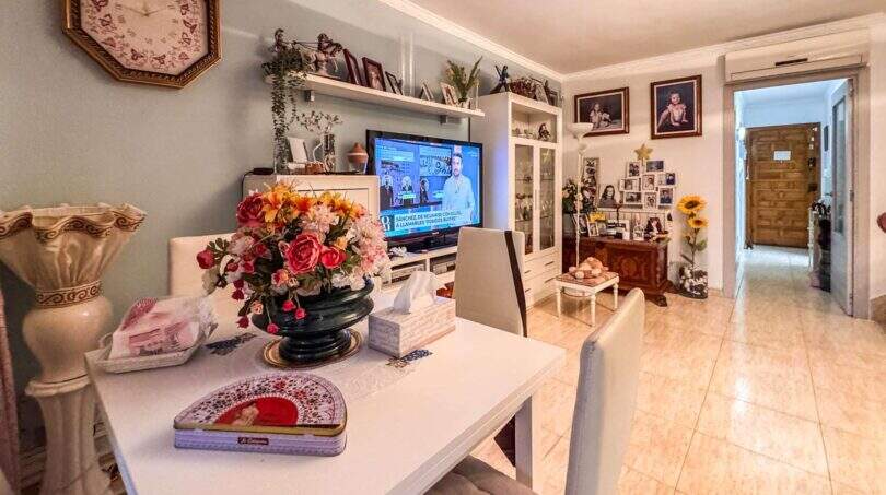 Wohnzimmer der Wohnung in Palma mit TV-Wand, Esstisch, Blumendeko und Familienfotos an der Wand.