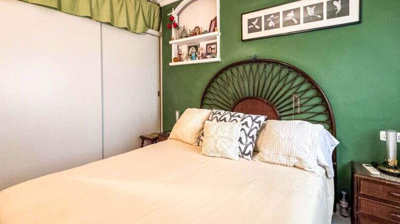 Schlafzimmer mit grüner Wand, Rattanbett, weißer Bettwäsche und Einbauschrank in strandnaher Wohnung Palma