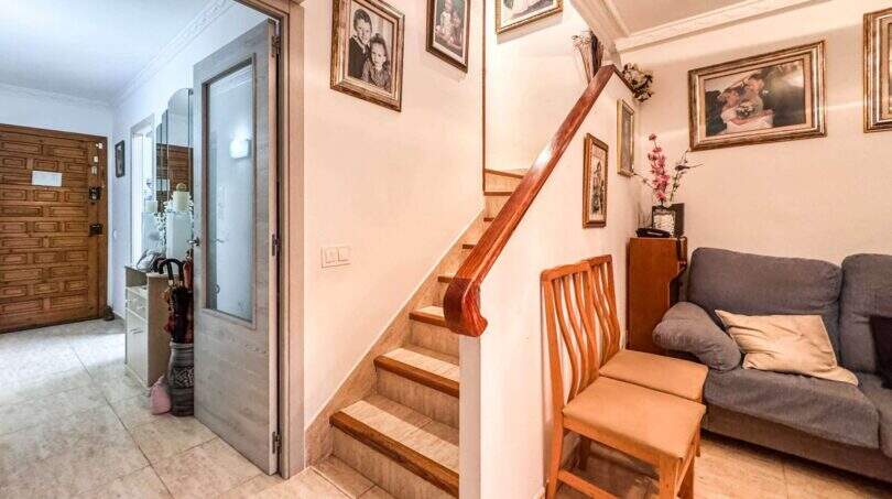 Eingangsbereich mit Holztreppe, Familienfotos, Sofa und Holztür in strandnaher Wohnung in Palma de Mallorca.
