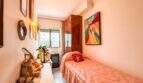Kleines Schlafzimmer mit Einzelbett, rosa Bettwäsche, buntem Gemälde und Holzschrank in strandnaher Palma-Wohnung