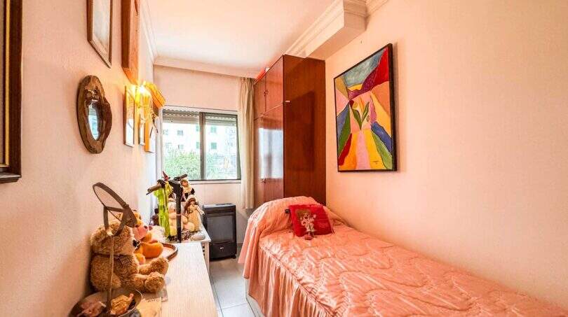Kleines Schlafzimmer mit Einzelbett, rosa Bettwäsche, buntem Gemälde und Holzschrank in strandnaher Palma-Wohnung