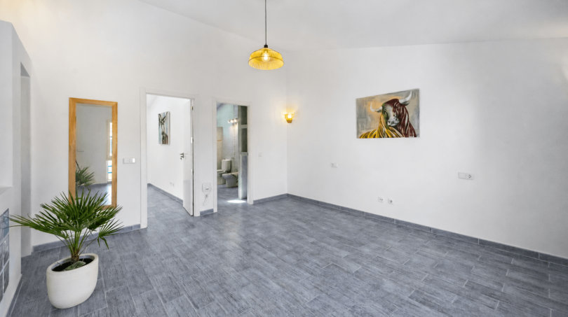 Helles Wohnzimmer mit grauem Fliesenboden, Pendelleuchte, Stiergemälde und Palme in Felanitx
