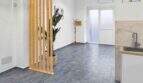 Modernes Wohnzimmer mit Holzraumteiler, Grünpflanze, grauem Fliesenboden und Miniküche in renoviertem Stadthaus Felanitx