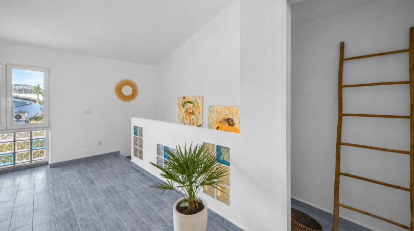 Heller Flurbereich mit grauem Fliesenboden, Kunstwerken, Palme und Holzleiter im Stadthaus Felanitx