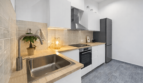 Moderne L-Küche mit Holzarbeitsplatte, Einbauofen, Edelstahlspüle und grauem Kühlschrank im Stadthaus Felanitx