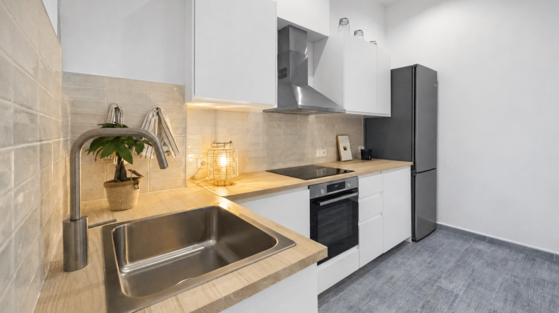 Moderne L-Küche mit Holzarbeitsplatte, Einbauofen, Edelstahlspüle und grauem Kühlschrank im Stadthaus Felanitx