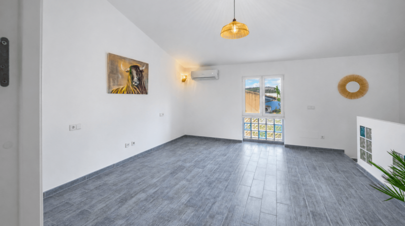 Helles, leeres Wohnzimmer mit grauem Fliesenboden, Klimaanlage, Pendelleuchte und Kunstwerk im Stadthaus Felanitx