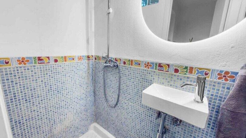 Modernes Bad mit blauem Mosaikfliesenspiegel, buntem Bordürendekor, Handbrause und elegantem Wandwaschbecken