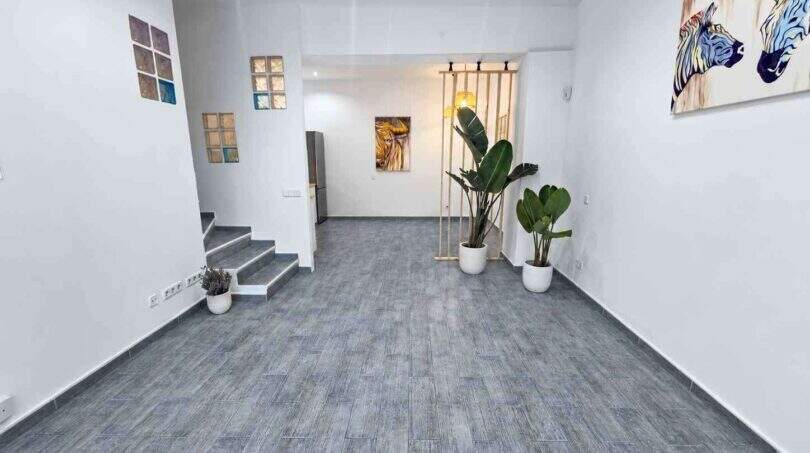 Helles Wohnzimmer mit grauem Fliesenboden, Treppe, tropischen Pflanzen und modernen Kunstwerken an weißen Wänden