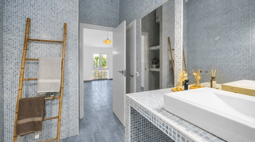 Modernes Badezimmer mit blauem Mosaikfliesen, Bambusleiter als Handtuchhalter und weißem Aufsatzwaschbecken in Stadthaus Felanitx