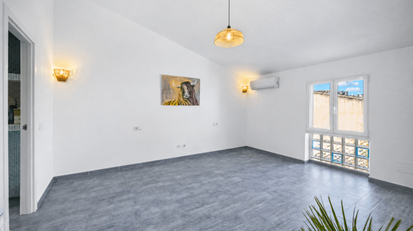Helles, leeres Wohnzimmer mit grauem Fliesenboden, Wandleuchten, Klimaanlage und Stierbild in Felanitx