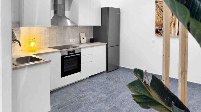 Moderne weiße Küche mit Einbauofen, Induktionskochfeld, Edelstahlkühlschrank und grauem Fliesenboden im Stadthaus Felanitx