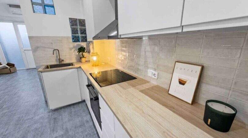 Moderne weiße Einbauküche mit Holzarbeitsplatte, Induktionskochfeld und Glasziegel-Rückwand im Stadthaus Felanitx