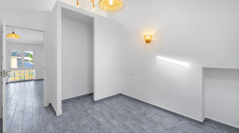 Heller, leerer Wohnraum mit grauem Fliesenboden, weißen Wänden und stilvollen Rattanlampen im renovierten Stadthaus Felanitx