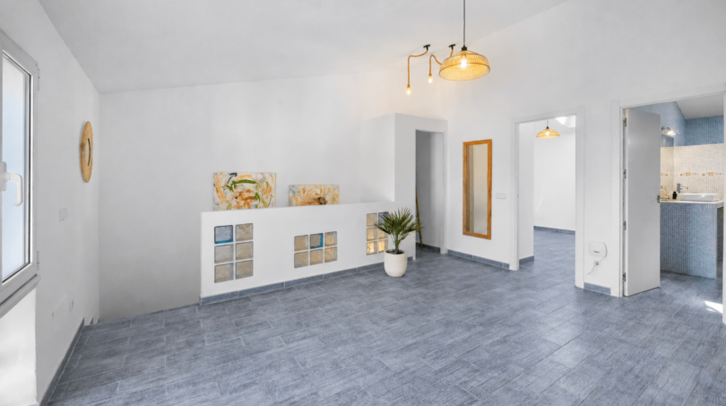 Helles Wohnzimmer mit grauem Fliesenboden, weißen Wänden, Glasbausteinwand und moderner Pendelleuchte in Felanitx