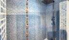 Badezimmer mit blauem Mosaikfliesenmuster, buntem Dekorstreifen und Duscharmatur über Badewanne