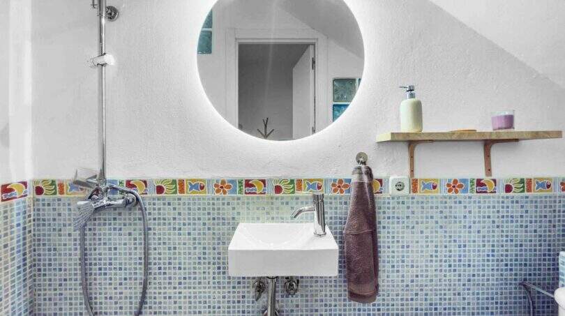 Modernes Badezimmer mit blauem Mosaikfliesenspiegel, buntem Fliesenbordüre und rundem LED-Spiegel im Stadthaus Felanitx